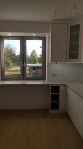 Biała kuchnia z jasno-marmurkowym blatem oraz czarnym AGD z frezowanymi uchwytami we frontach.