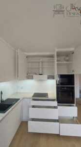 Biała kuchnia z jasno-marmurkowym blatem oraz czarnym AGD z frezowanymi uchwytami we frontach.