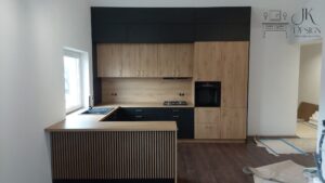 Duża kuchnia w zabudowie z wysokim ukośnym sufitem. Synergia dębu oraz czerni wraz z miedzianymi uchwytami oraz lamele.