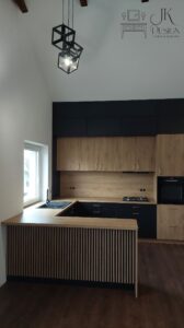 Duża kuchnia w zabudowie z wysokim ukośnym sufitem. Synergia dębu oraz czerni wraz z miedzianymi uchwytami oraz lamele.