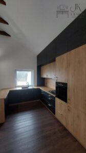 Duża kuchnia w zabudowie z wysokim ukośnym sufitem. Synergia dębu oraz czerni wraz z miedzianymi uchwytami oraz lamele.